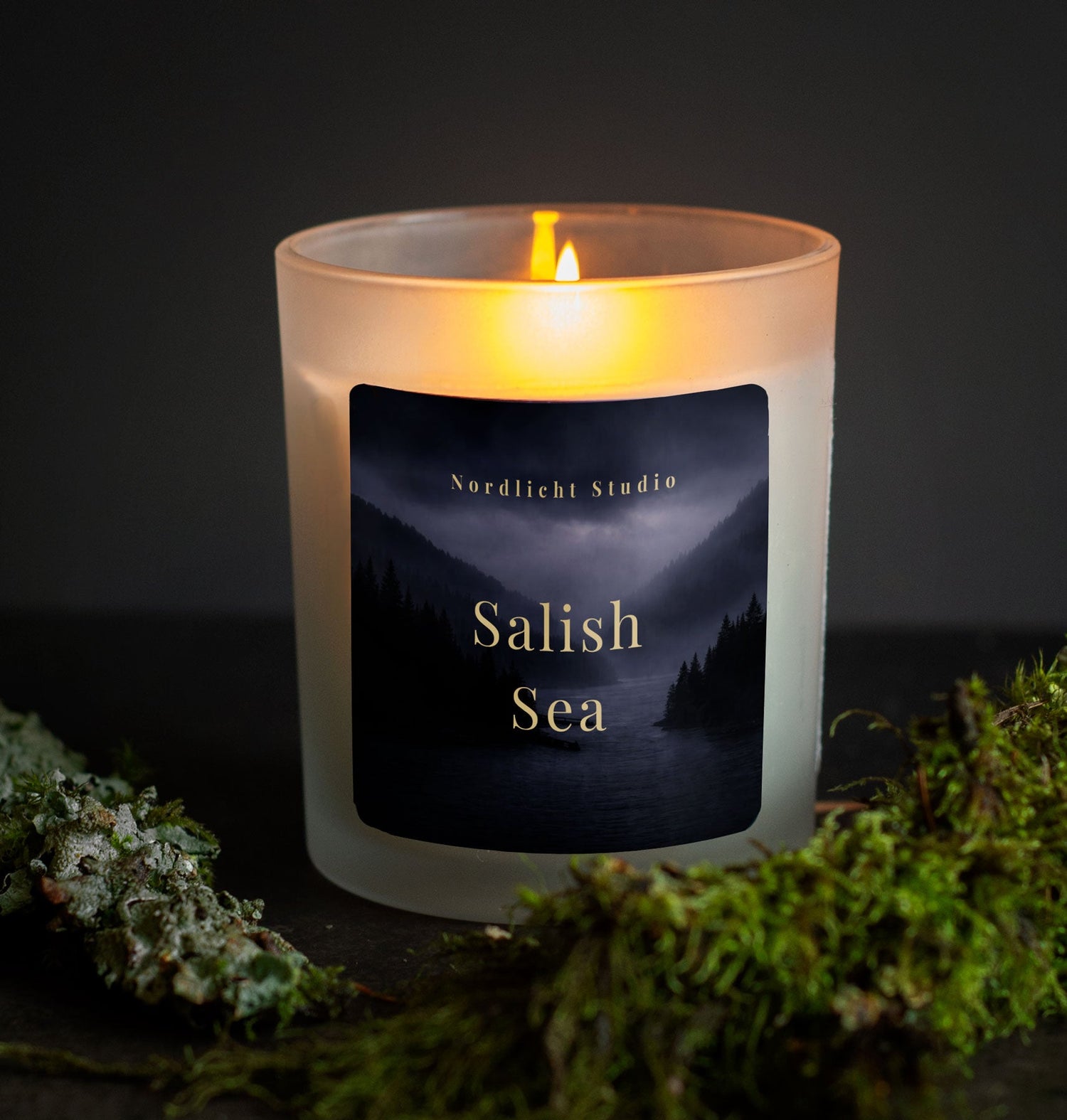 burning candle in a frosted jar surrounded by lichen on a branch